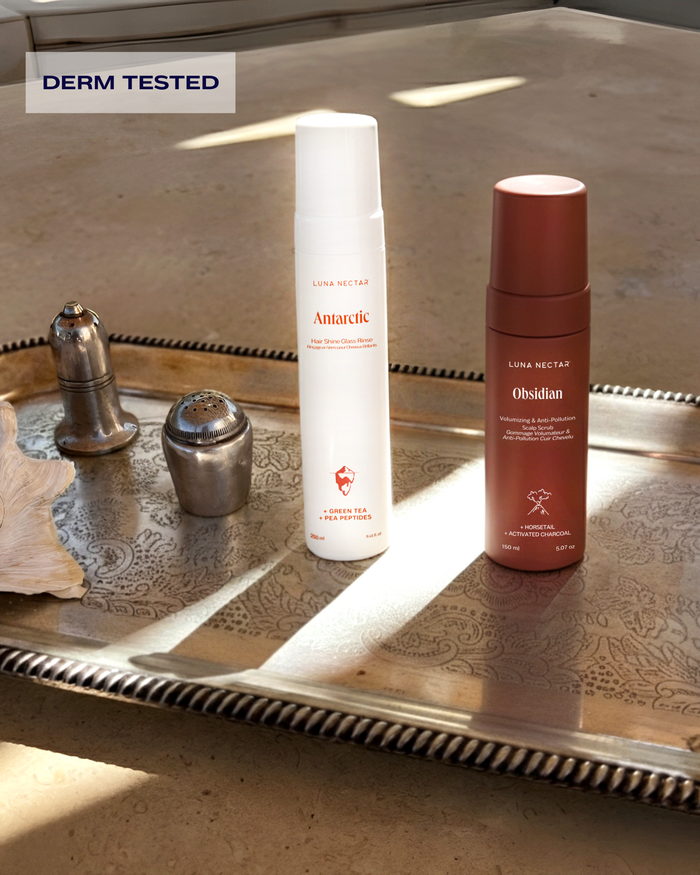 Antarctic hair shine rinse and Obsidian volumizing scalp scrub bottles displayed together on a silver tray, derm-tested