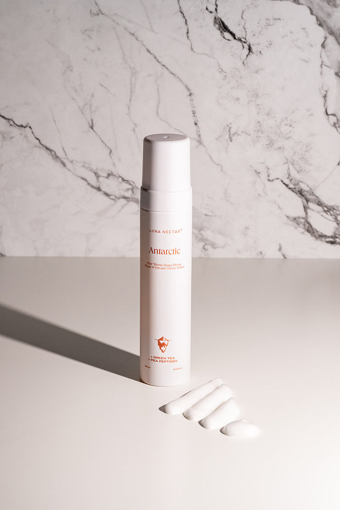 Antarctic hair shine glass rinse bottle with a texture swatch showing its lightweight white lotion
